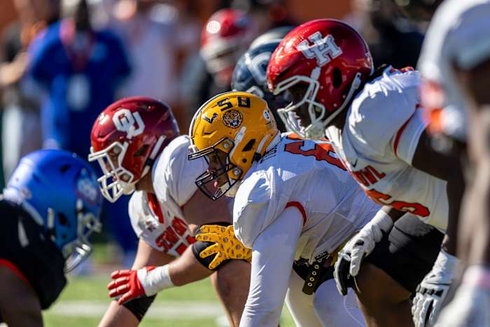 Various linemen bend over to prepare for the snap, with OU, LSU and UH on their helmets